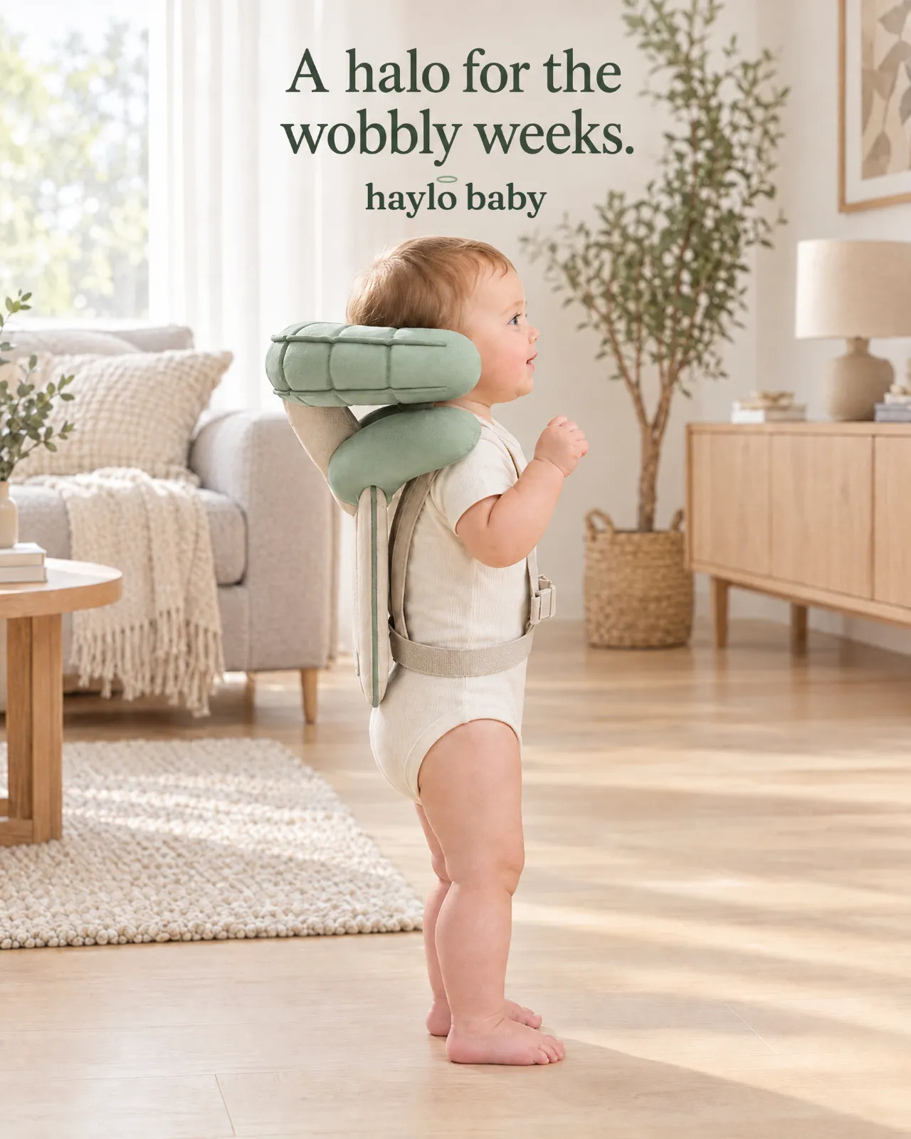 Baby standing in a living room wearing the Haylo Baby head cushion, with the line: A halo for the wobbly weeks