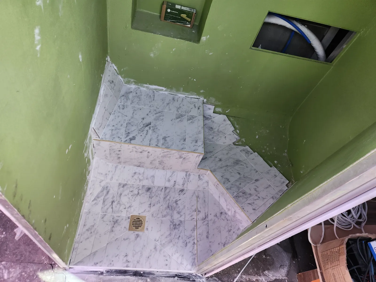 Marble tiles going down — gold drain in place, green walls still visible