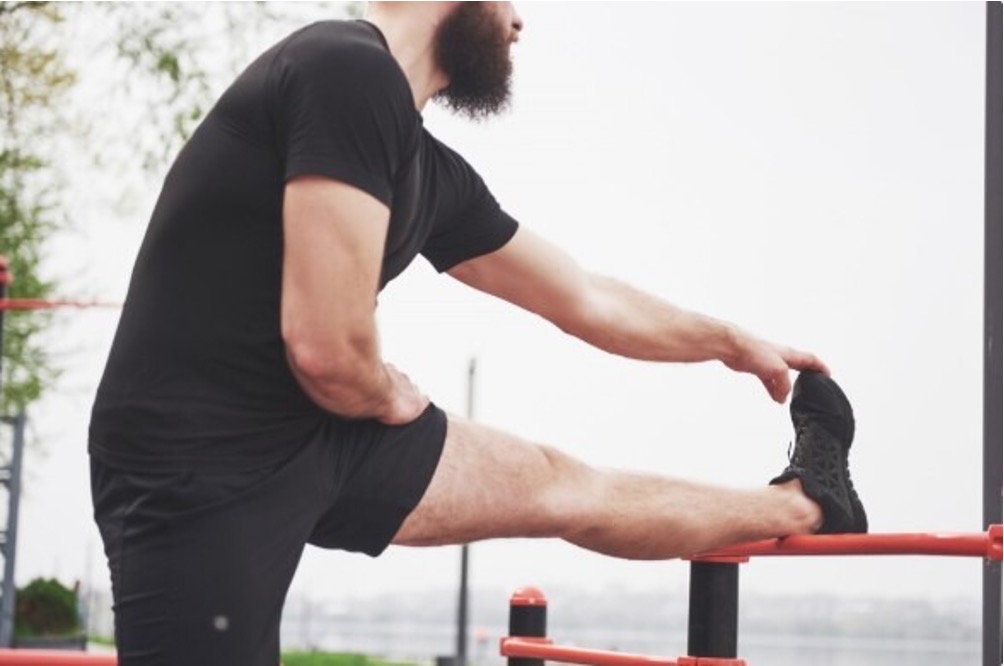 Man in black activewear stretching his muscles on an outdoor exercise bar.