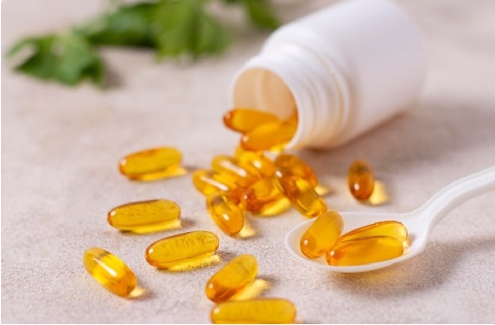 Golden softgel capsules spilling from a white bottle onto a spoon.