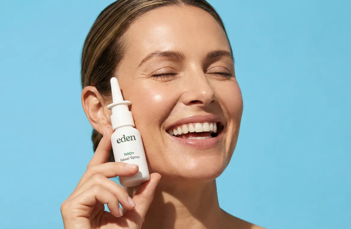 Smiling woman holding a bottle of Eden NAD+ Nasal Spray against a blue background.