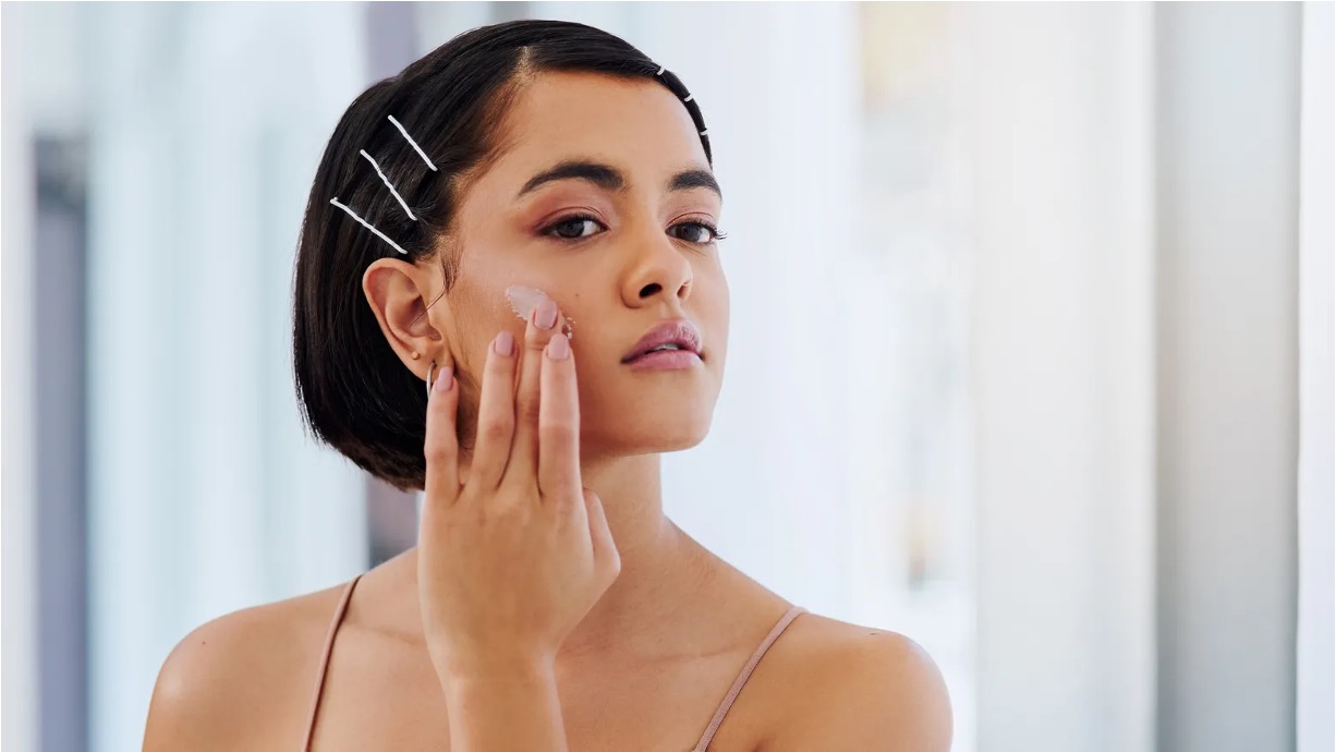 Woman with hair pinned back pressing serum into her cheekbone, demonstrating correct peptide application technique