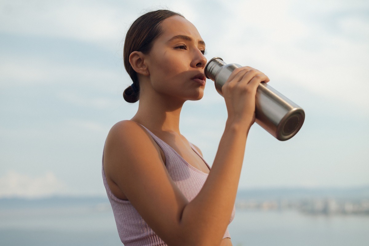 Woman drinking water from a metal bottle outdoors to maintain hydration during sports recovery