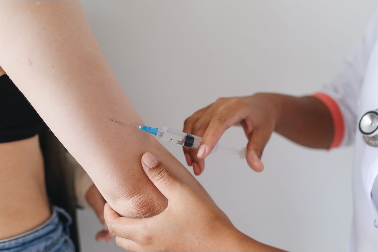 Clinician in white coat preparing to give an injection in a person's upper arm