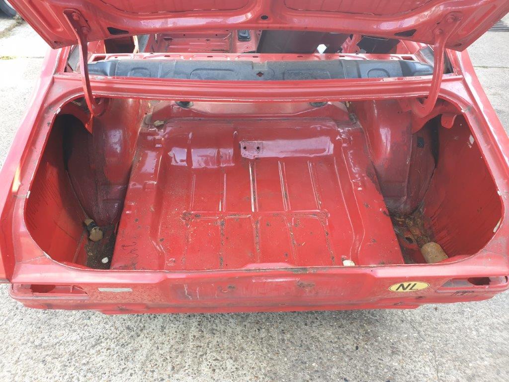 The bare interior floor of the red Escort shell, trim already removed