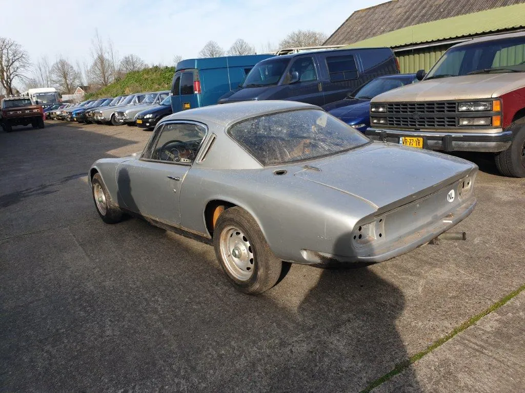 The Lotus Elan 2+2 photographed from the rear three-quarter, parked among other cars on the yard