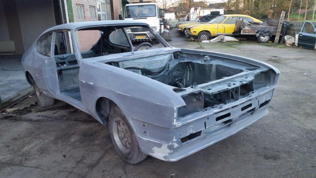 The Capri shell in primer on the yard, doors and bonnet removed, front three-quarter view
