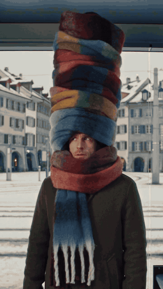 Person trÀgt einen riesigen Stapel Schals auf dem Kopf auf einem winterlichen Stadtplatz