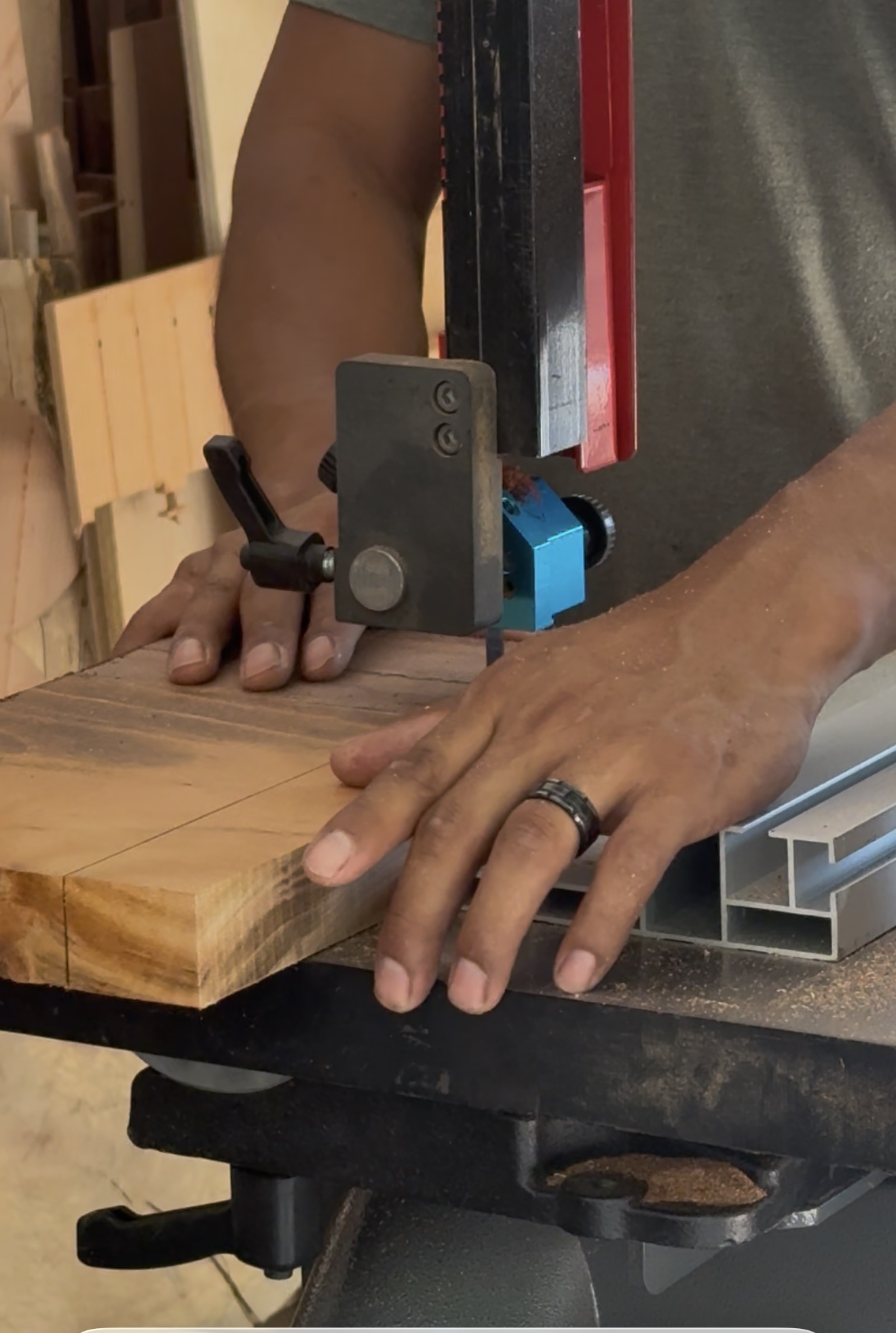 Hands guiding a hardwood board through a bandsaw in the workshop