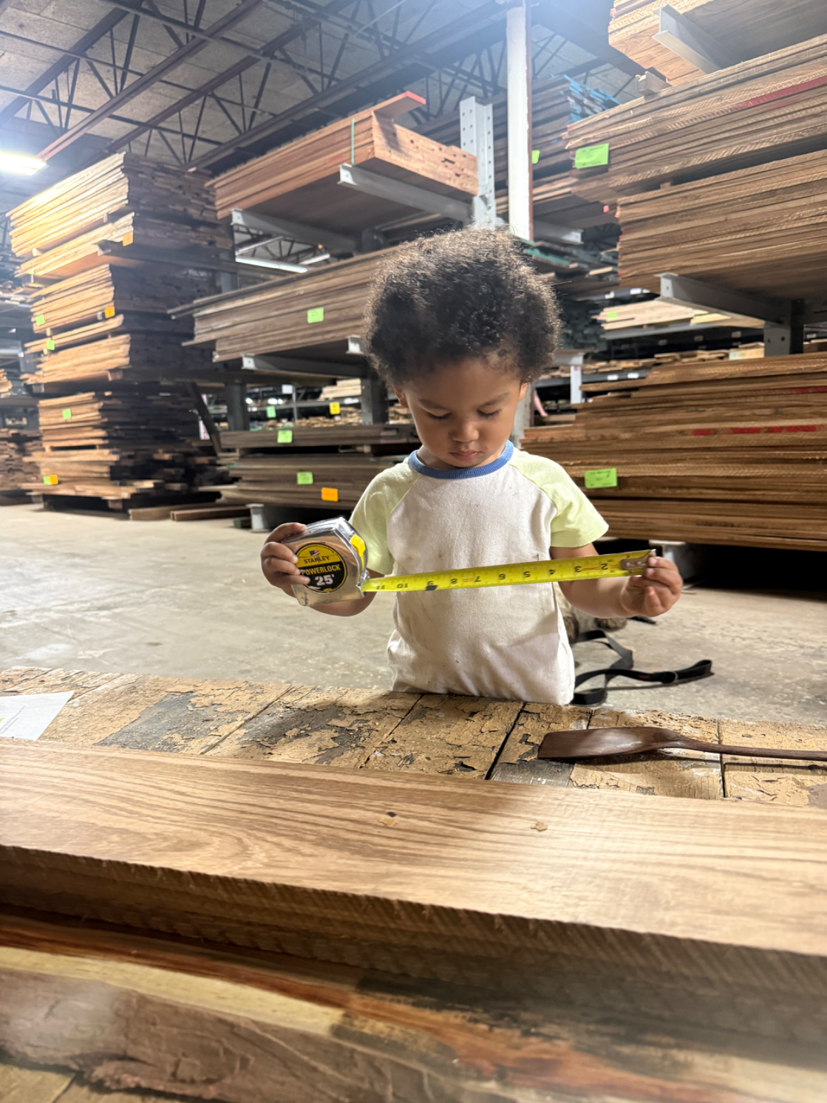 A small child measuring a hardwood slab with a tape measure at the lumberyard