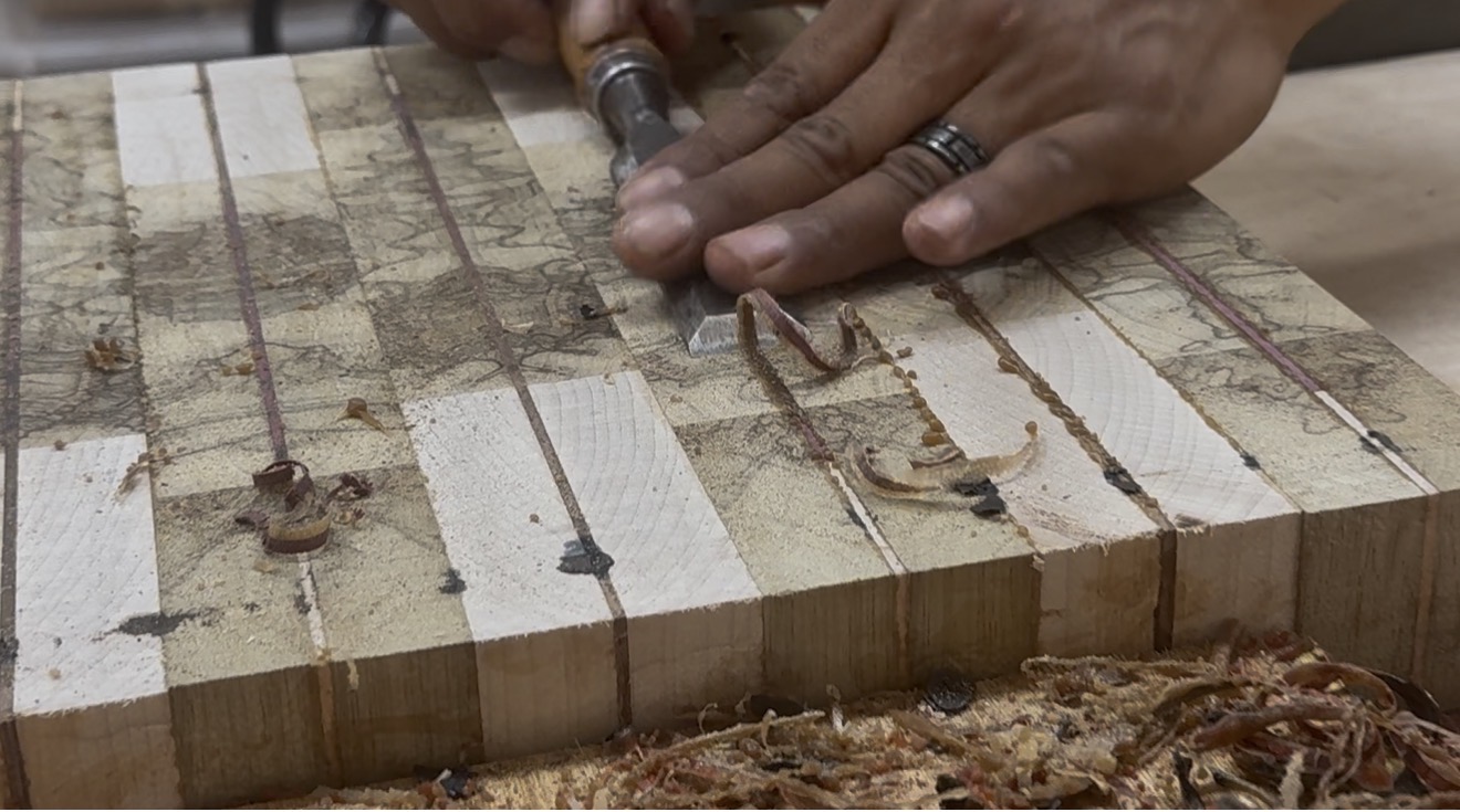 Hands paring the inlay of an end-grain cutting board with a chisel