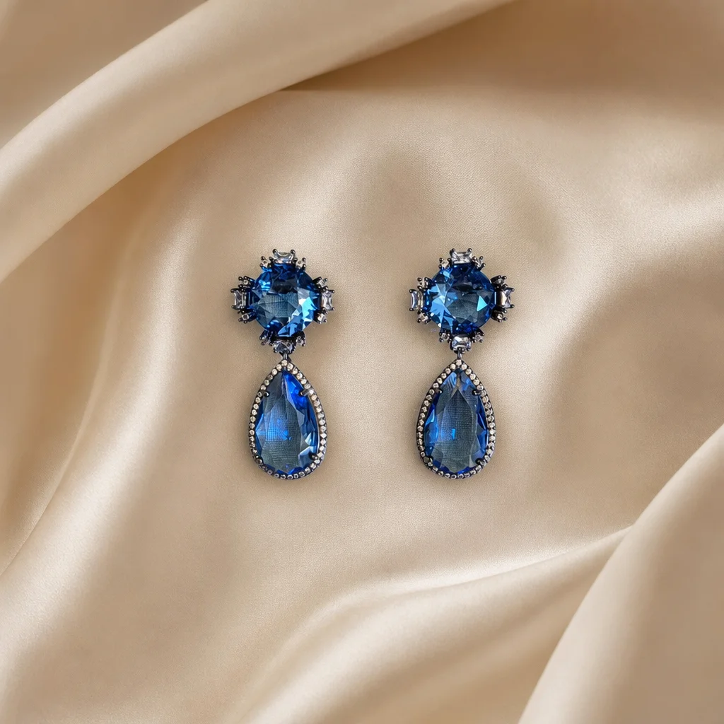 Pedra azul redonda rodeada de cristais e gota azul pendente cravejada.