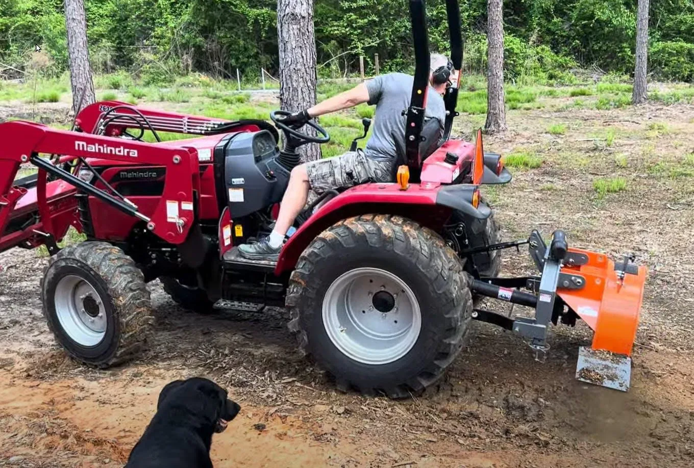 The SG24 grinder mounted on a red Mahindra compact tractor with the operator turned to watch the wheel