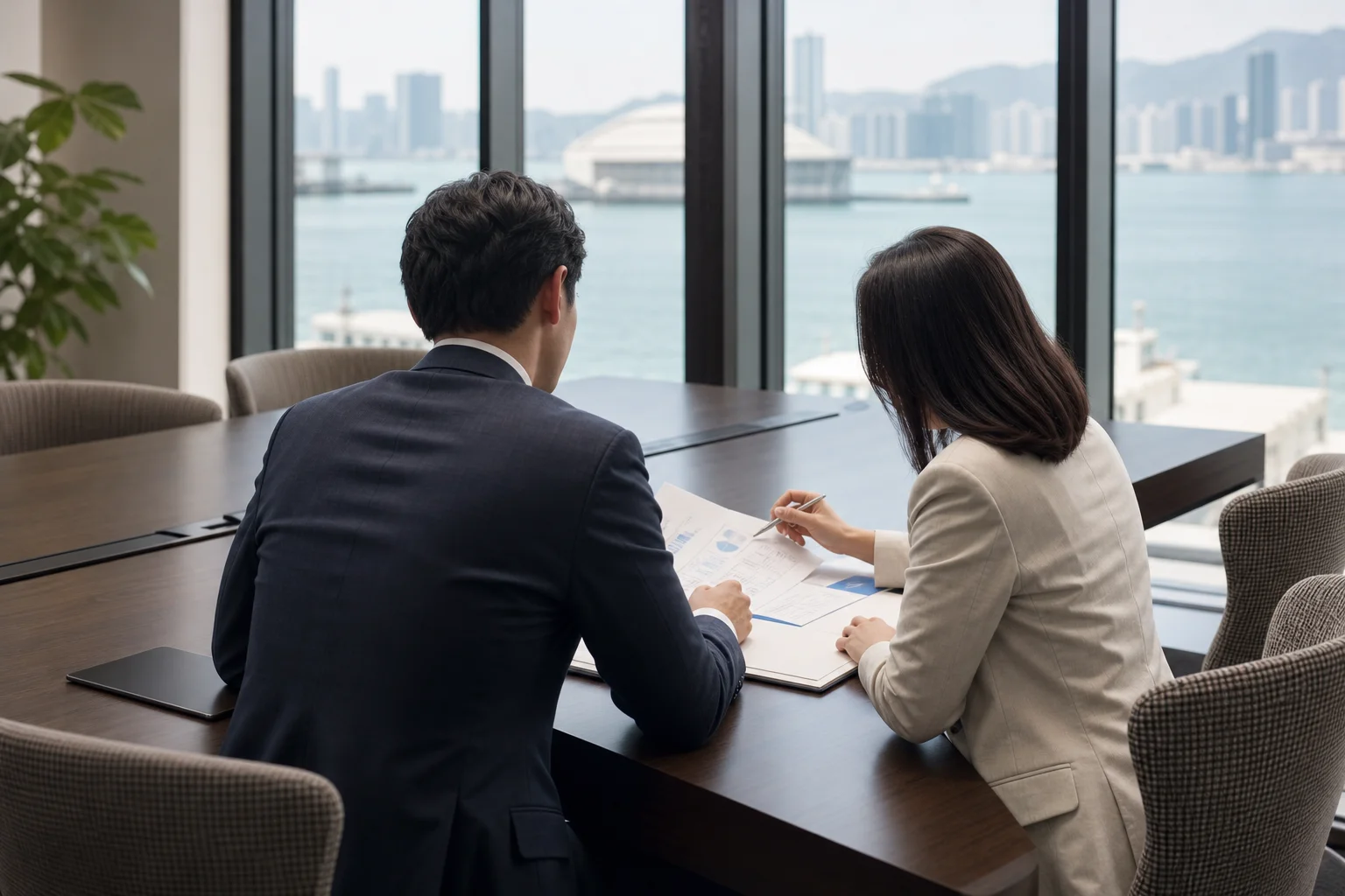 Two colleagues reviewing documents at a meeting table in an office overlooking a harbour